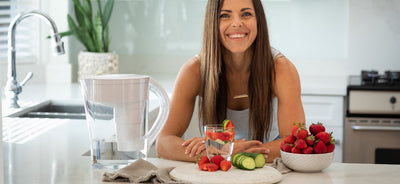 Woman smiling while leaning on her kitchen counter in front of a glass of Santevia Alkaline Mineral Water