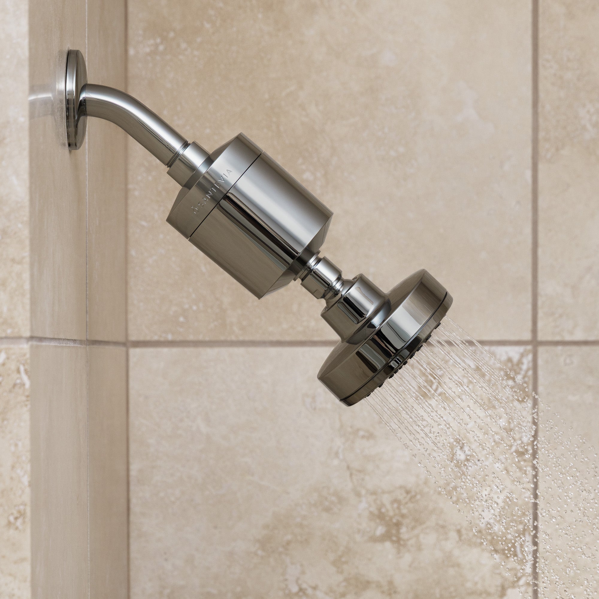 Chrome shower head on a tiled wall with water flowing.