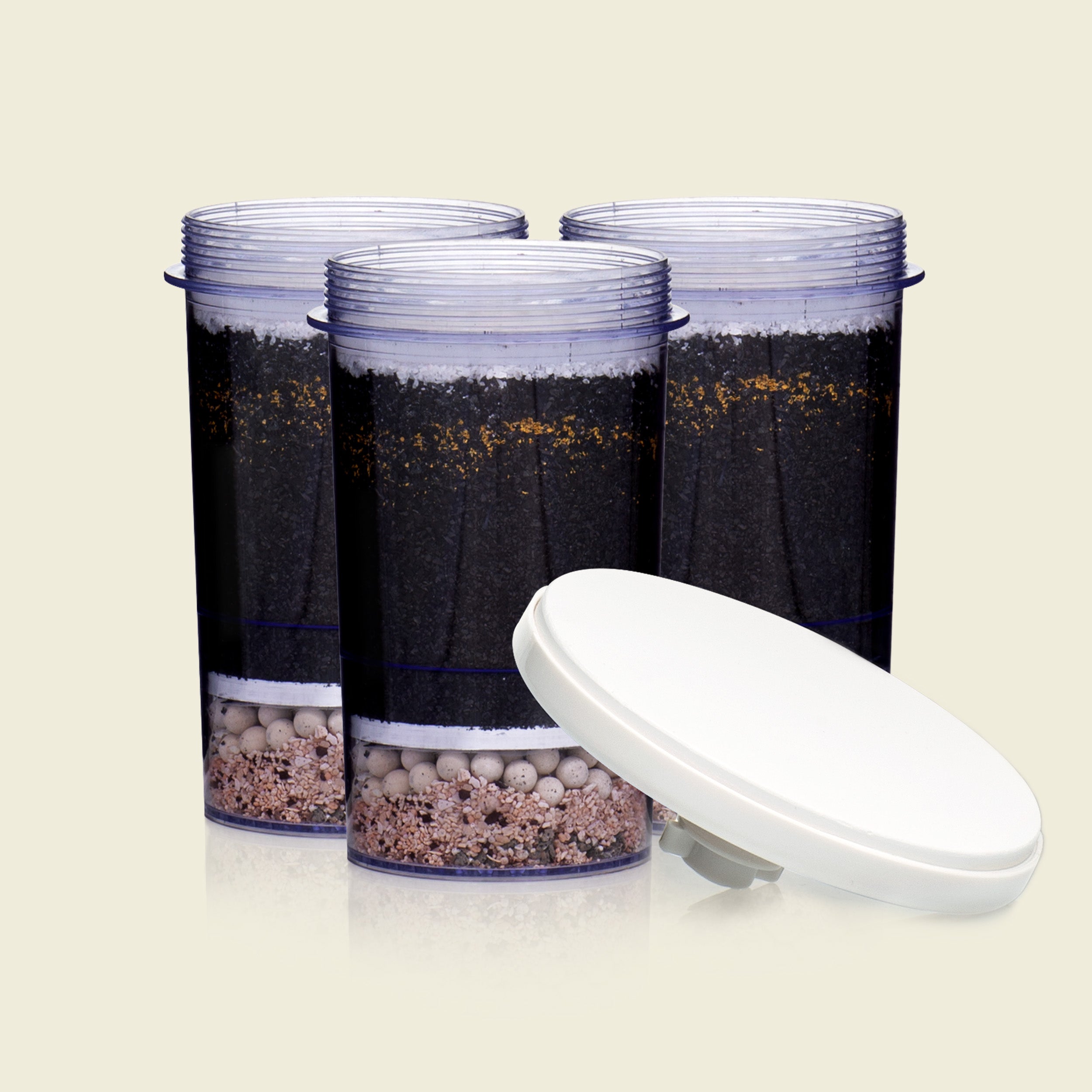 Three cylindrical containers with soil and small stones, accompanied by a white lid on a beige background.