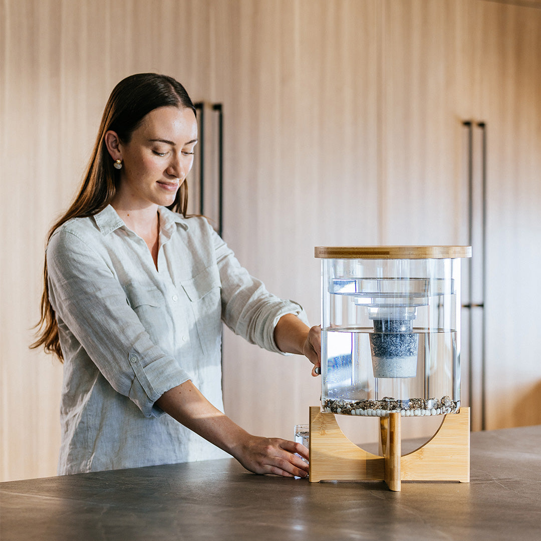 Woman pouring a glass of water from a Santevia Glass Water System in a warm kitchen