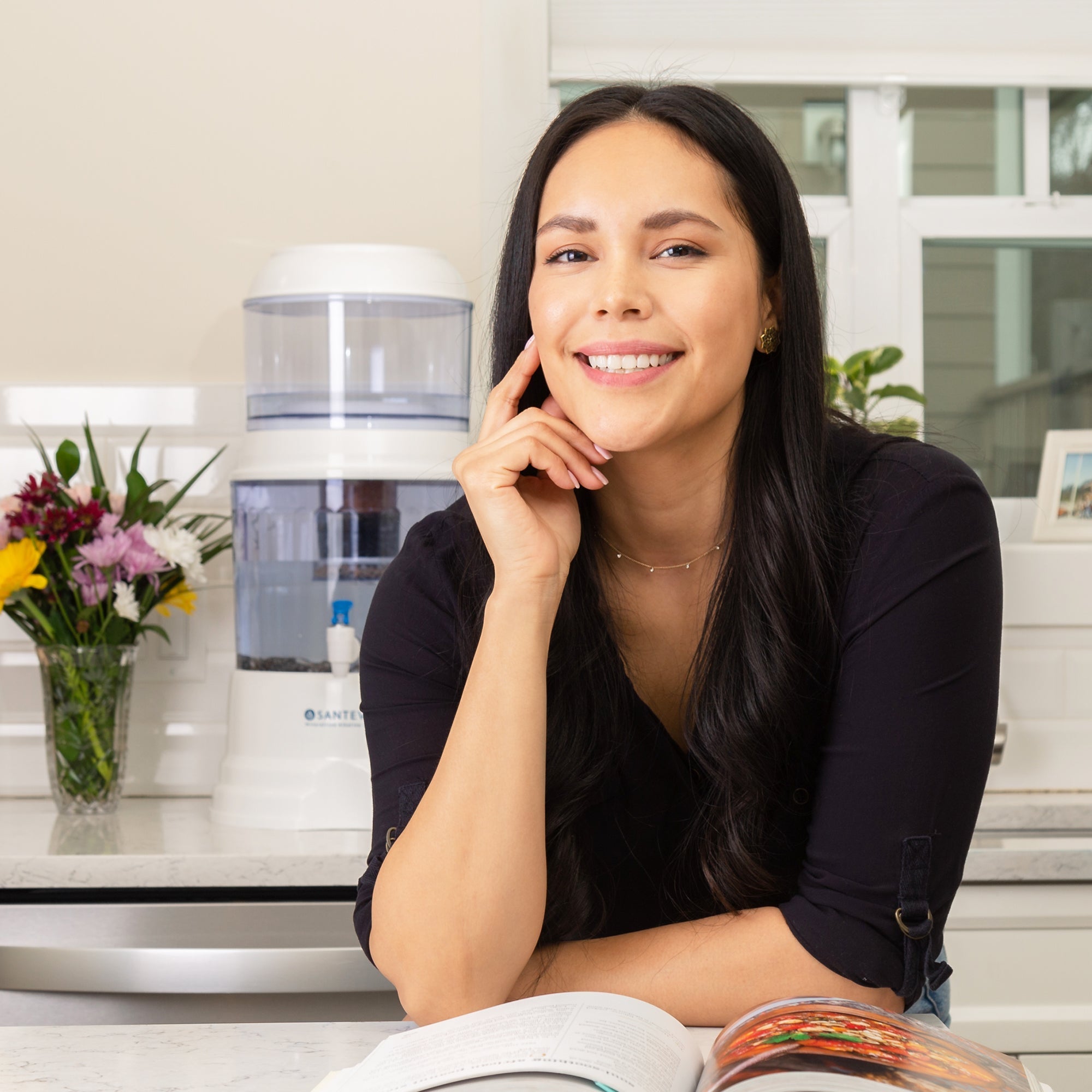 A woman reading a healthy cooking book and smiling in front of her Santevia Gravity Water System