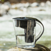 The Santevia MINA Alkaline Pitcher in Black sitting on top of a rock facing a Canadian river