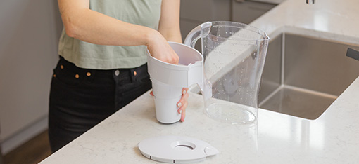A woman standing by the kitchen sink while chaning her Santevia MINA Alkaline Water Pitcher Filter