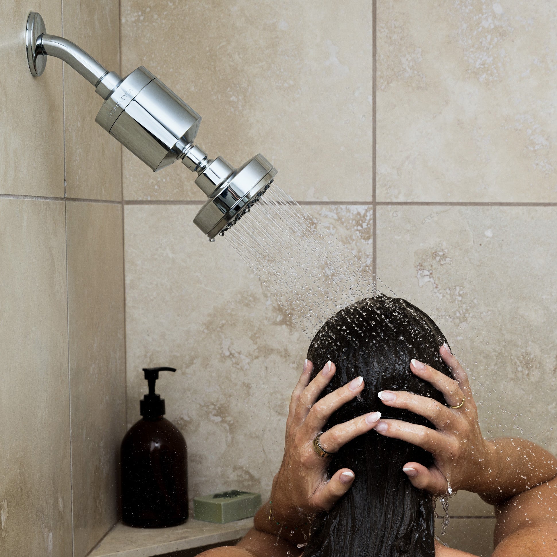 Person showering with a handheld showerhead in a tiled bathroom.