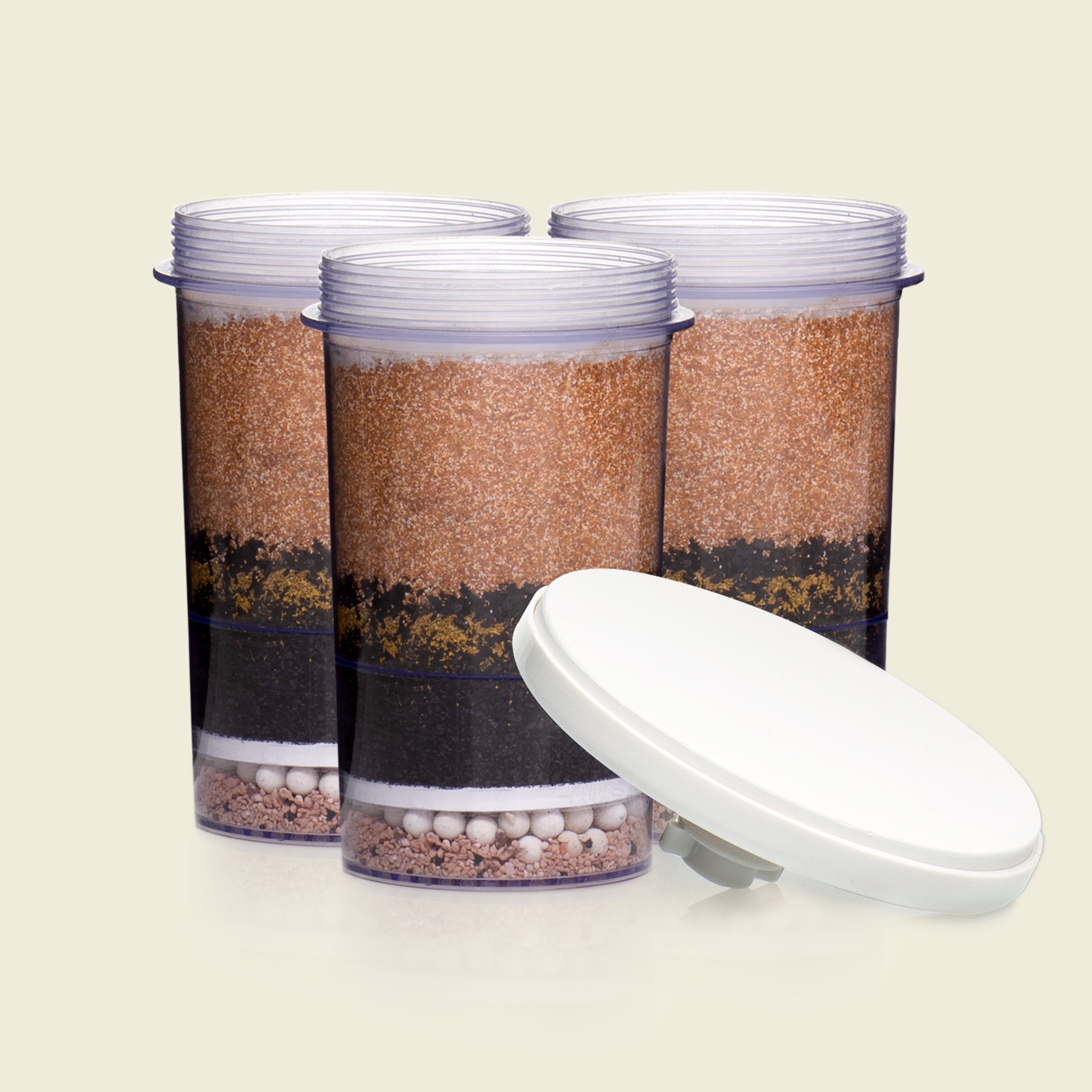 Three cylindrical containers with layered contents and a white lid on a beige background