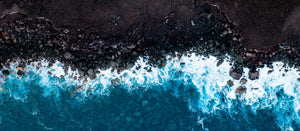 aerial shot of a water crashing onto a dark shoreline