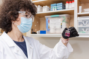 A chemist in a lab making observation of a vial of pink solution