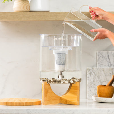 glass pitcher pouring water into a Santevia Glass Water System in a white marble kitchen