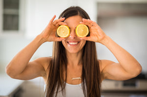 Woman smiling while holding a round slice of lemon over each eye